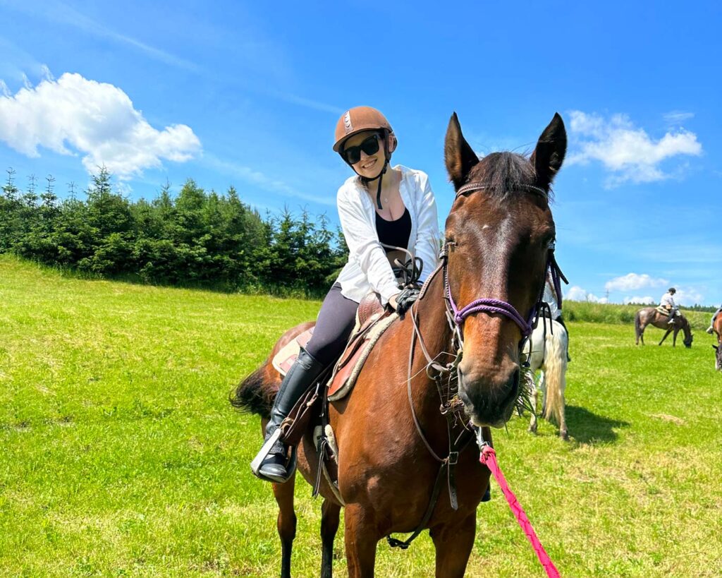 A woman smiling joyfully while riding a brown horse in a lush green field, representing the freedom and achievement users experience by navigating their life's paths with the Dream Map.